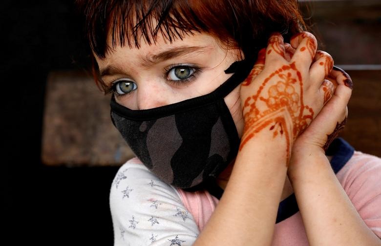 Tasmina, 4, adjusts her protective face mask as she waits with her family for a train at a railway station in Karachi, Pakistan June 9. REUTERS/Akhtar Soomro